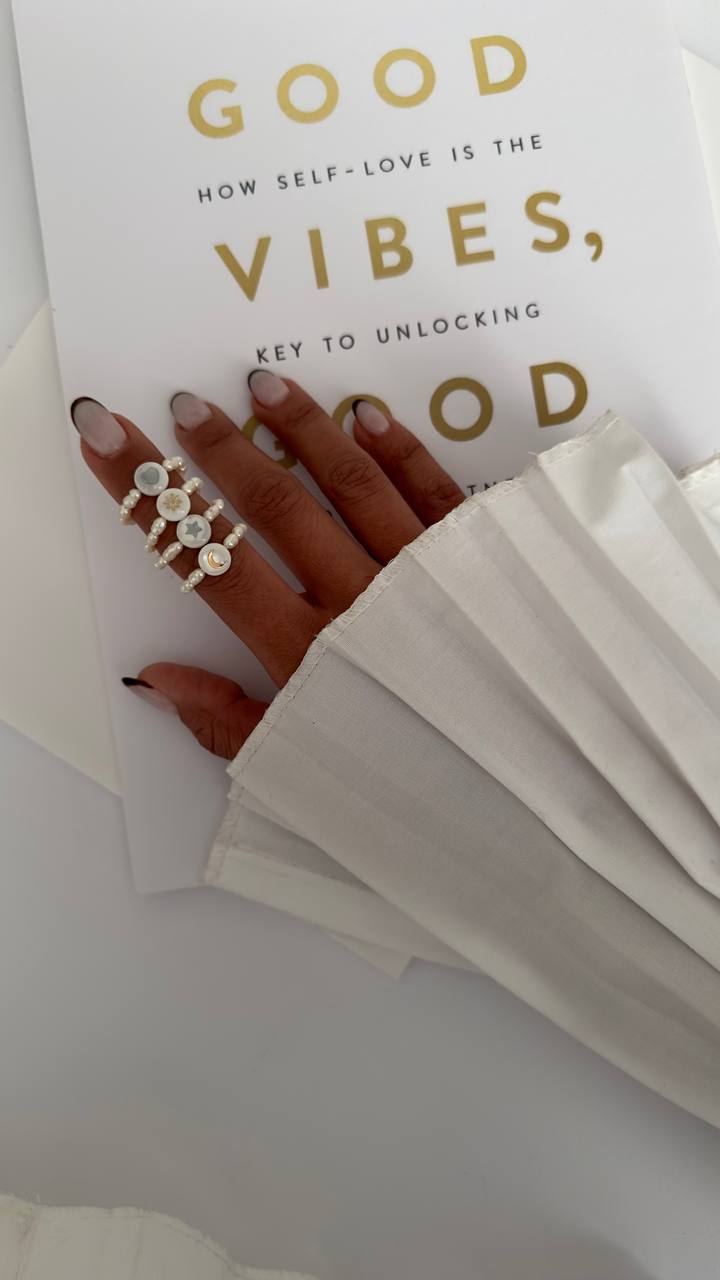 Hand with multiple rings holding a book titled 'Good Vibes, Key to Unlocking Good' on a white background