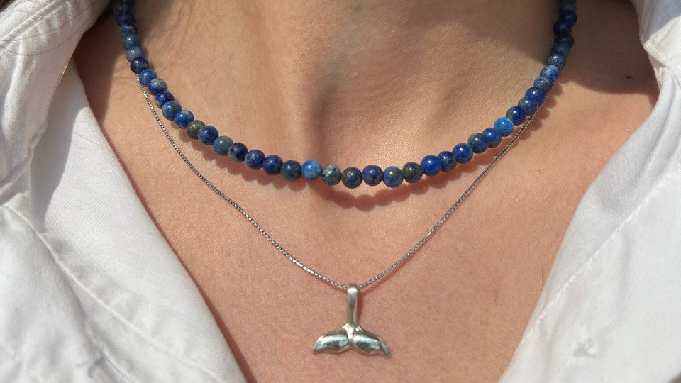 Close-up of a person wearing a blue beaded necklace and a silver whale pendant necklace.