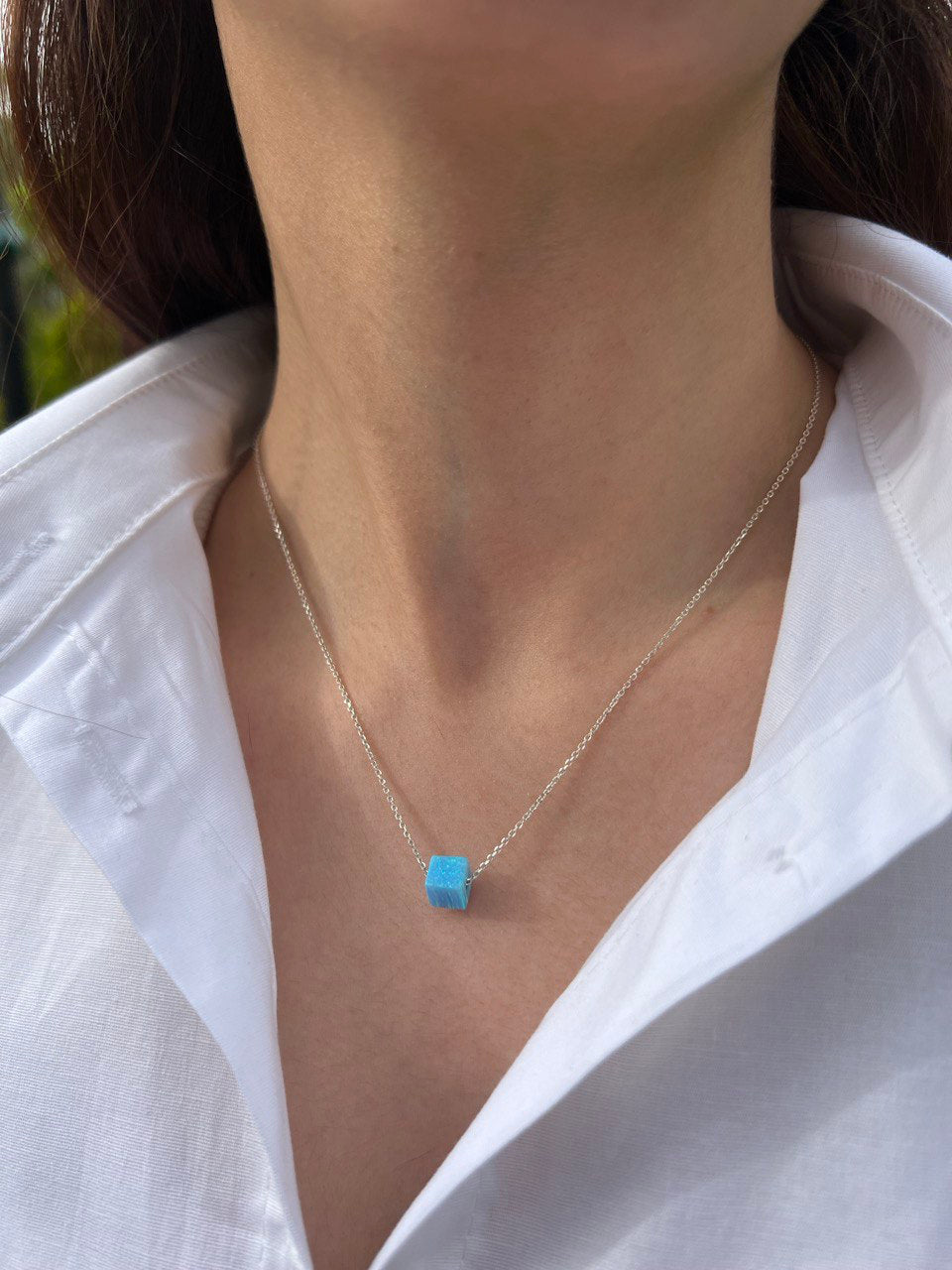 Necklace with a blue pendant worn by a person in a white shirt.