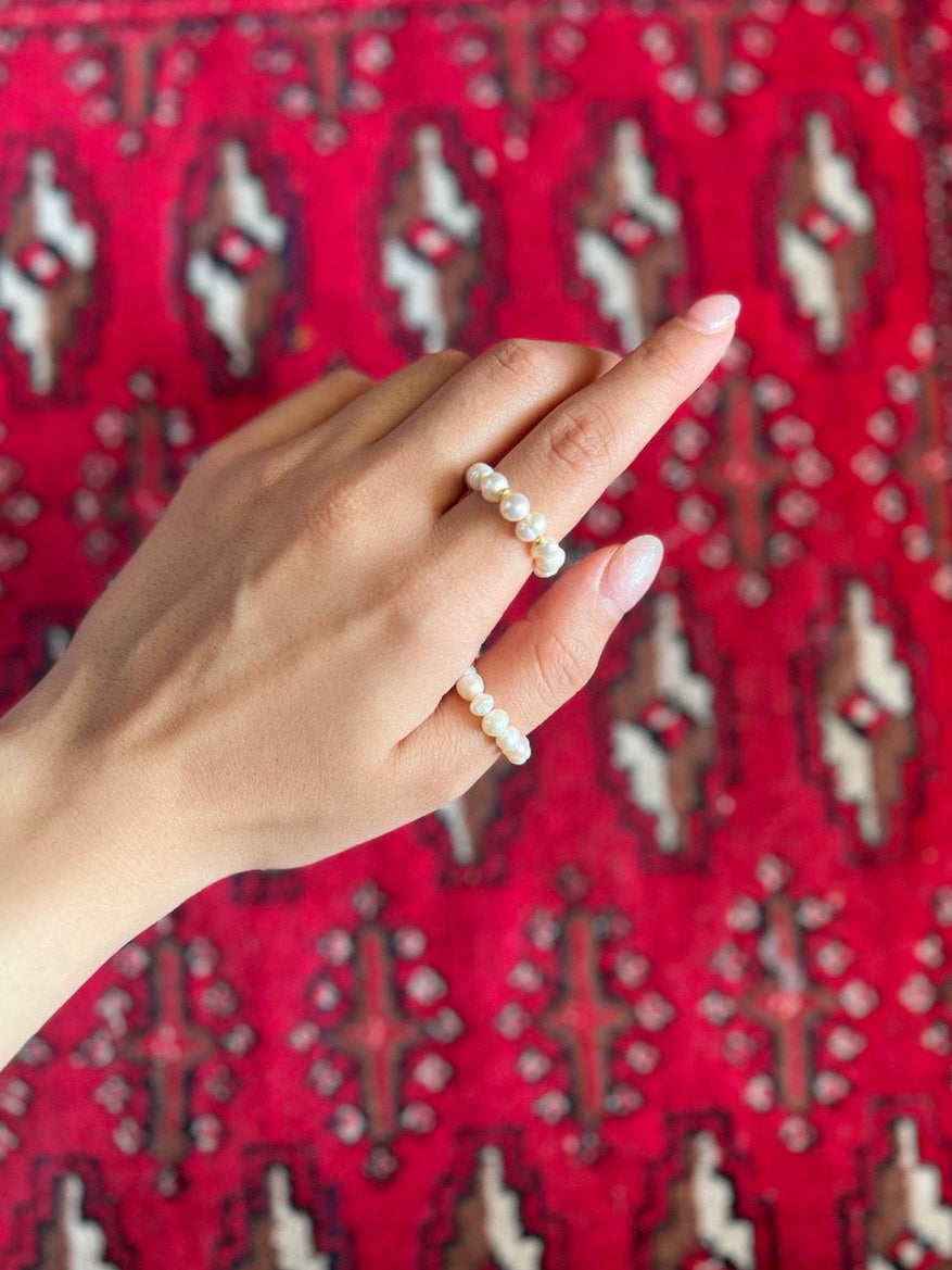 Hand wearing a pearl ring on a red patterned fabric background